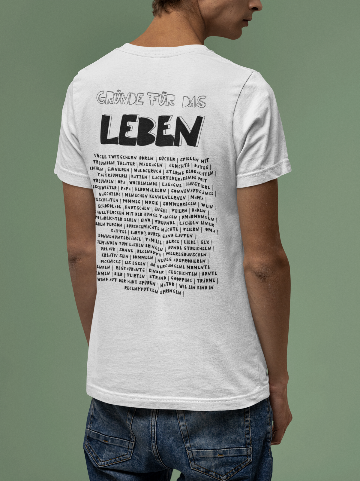 Männliches Modell vor grünem Hintergrund. Modell trägt weißes handgedrucktes Shirt mit dem Motiv Gründe für das Leben