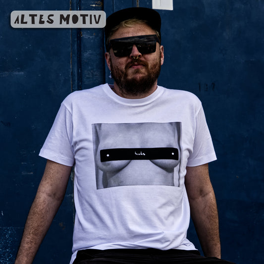 Männliches Modell vor blauem Hintergrund. Er trägt ein weißes Shirt mit dem Motiv "boobs 2.0" in schwarz.