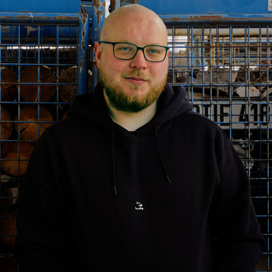 Männliches Modell vor Holzcontainer. Model trägt schwarzen Hoodie mit dem weißen Aufdruck boobs.